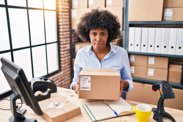 Black woman with curly hair working at small business ecommerce holding box depressed and worry for distress, crying angry and afraid. sad expression.  - Fotoğraf, Görsel