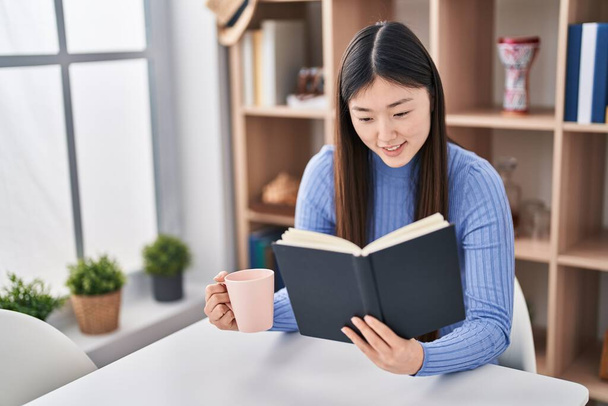 Chinese vrouw die boek leest en thuis koffie drinkt - Foto, afbeelding