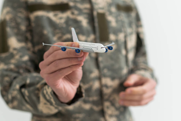 Military Technical Service, Air Force Concept. Hands of a man in uniform holding a silver toy airplane. A middle-aged adult man in a green camouflage uniform. Indoors. Selective Focus. Low key. - Foto, immagini