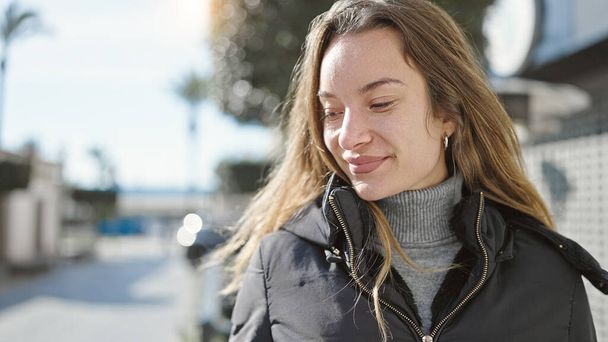 jonge Kaukasische vrouw glimlachen zelfverzekerd naar beneden te kijken op straat - Foto, afbeelding