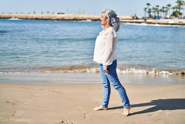 Женщина средних лет уверенно улыбается стоя на берегу моря - Фото, изображение