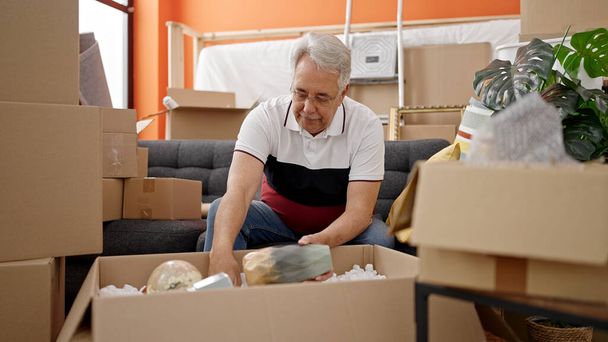 Hombre de mediana edad con pelo gris desembalaje caja de cartón en el nuevo hogar - Foto, imagen