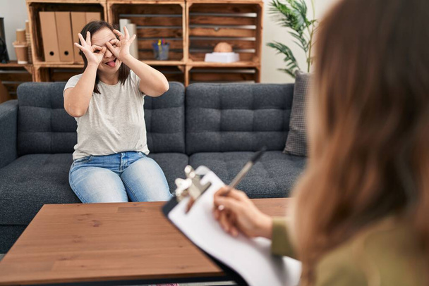 Hispanic girl with down syndrome doing therapy doing ok gesture like binoculars sticking tongue out, eyes looking through fingers. crazy expression.  - Photo, Image
