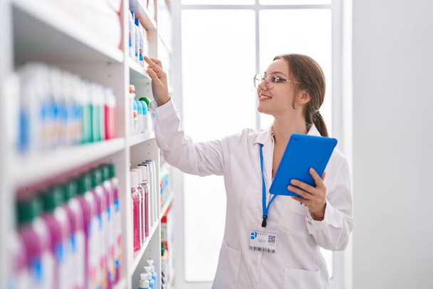 Jonge blonde vrouw apotheker met behulp van touchpad op zoek naar medicijnen bij de apotheek - Foto, afbeelding