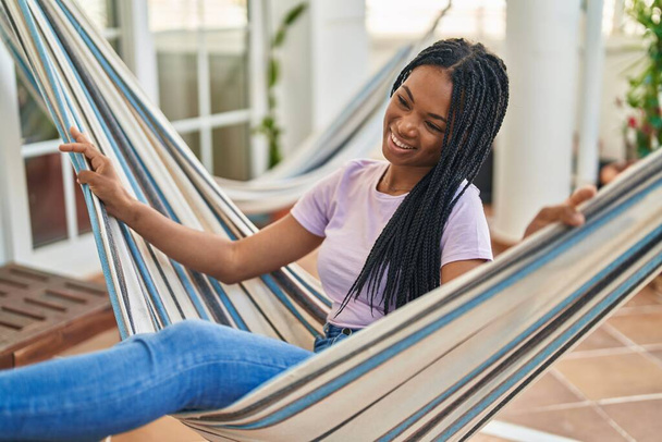 African american woman smiling confident swinging on hammock at home terrace - Valokuva, kuva