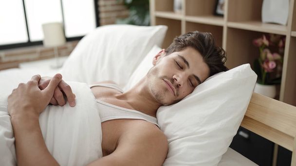 Young hispanic man lying on bed sleeping at bedroom - 写真・画像