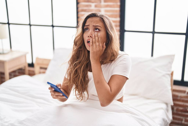 Young beautiful hispanic woman using smartphone with worried expression at bedroom - Фото, зображення