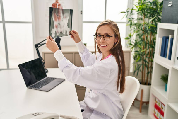 Giovane donna bionda medico utilizzando computer portatile in possesso di raggi X in clinica - Foto, immagini
