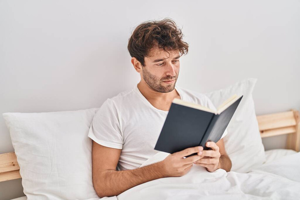 Fiatal férfi olvasás könyvet ül az ágyon a hálószobában - Fotó, kép
