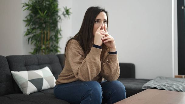 Schöne hispanische Frau sitzt auf Sofa mit Zweifel Ausdruck zu Hause - Foto, Bild