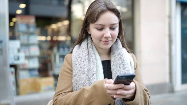 Jeune femme blonde souriant confiant en utilisant smartphone à la rue - Photo, image