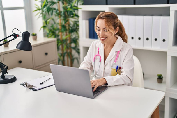 Young woman wearing doctor uniform using laptop working at clinic - Foto, imagen