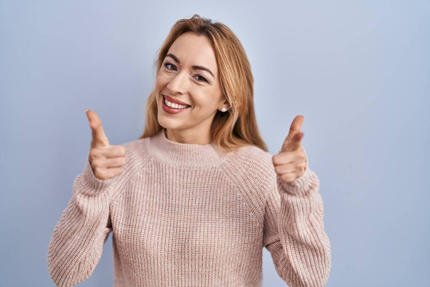 Hispanic woman standing over blue background pointing fingers to camera with happy and funny face. good energy and vibes.  - Foto, afbeelding