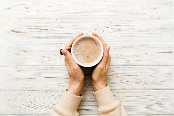 Minimalistic style woman hand holding a cup of coffee on Colored background. Flat lay, top view cappuccino cup. Empty place for text, copy space. Coffee addiction. Top view, flat lay. - Photo, Image