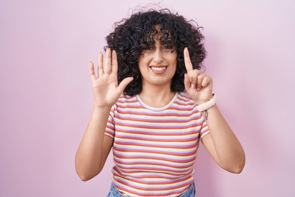 Jovem mulher do Oriente Médio em pé sobre fundo rosa mostrando e apontando para cima com os dedos número seis, enquanto sorrindo confiante e feliz.  - Foto, Imagem