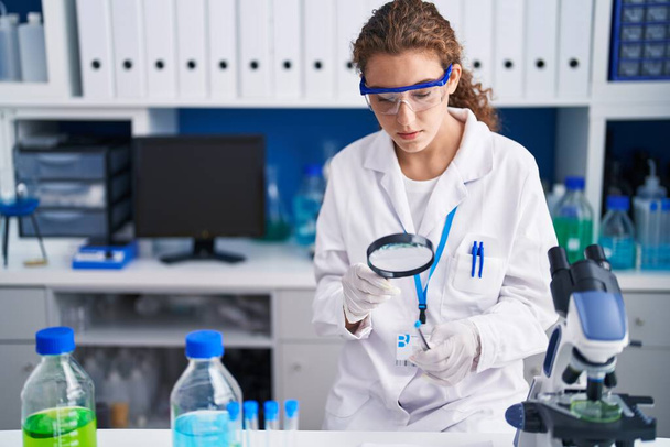 Joven mujer hispana hermosa científico buscando tubo de ensayo con lupa en el laboratorio - Foto, imagen