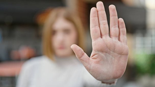 Young blonde woman doing stop gesture with hand at coffee shop terrace - Photo, image