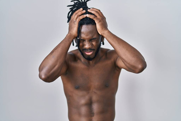 Африканский мужчина с дредами, стоящий без рубашки на изолированном фоне, страдающий от головной боли в отчаянии и стрессе из-за боли и мигрени. руки на голове.  - Фото, изображение