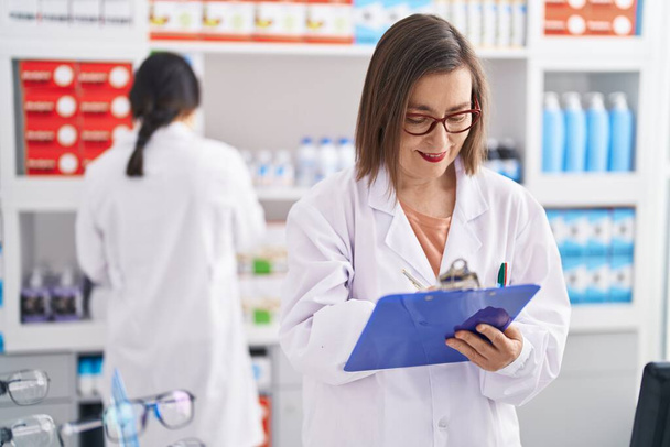Two women pharmacist smiling confident writing on document at pharmacy - Zdjęcie, obraz