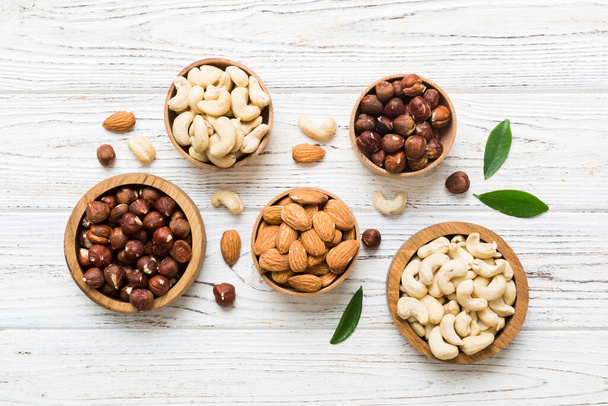 Assortment of nuts in wooden bowl on colored table. Cashew, hazelnuts, walnuts, almonds. Mix of nuts Top view with copy space. - Photo, Image