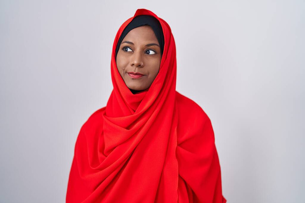 Jonge Arabische vrouw draagt traditionele islamitische hijab sjaal glimlachend naar de zijkant en staren weg denken.  - Foto, afbeelding