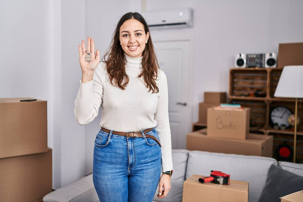 Young hispanic woman holding keys of new home looking positive and happy standing and smiling with a confident smile showing teeth  - Фото, изображение