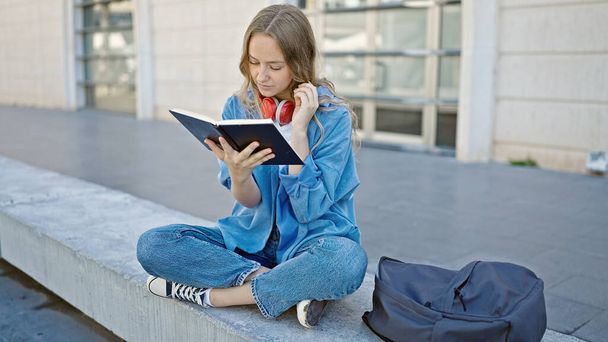 Young blonde woman student reading book sitting on bench at university - Photo, Image