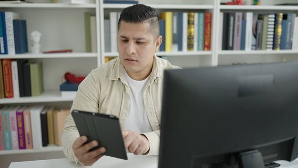 Young hispanic man student using computer and touchpad studying at library university - Фото, зображення