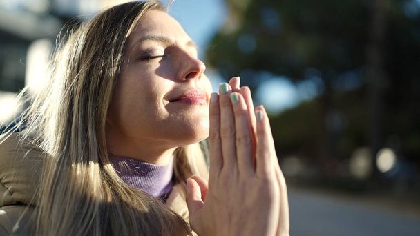 Young blonde woman praying with closed eyes at street - Photo, image