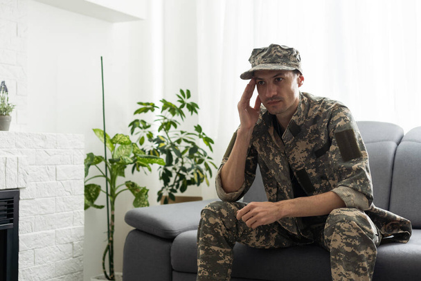 Sotilaspukuinen mies istuu tuolissa ikkunan vieressä. Konsepti: sotilas psykologin nimittämisessä, traumaperäinen stressioireyhtymä, mielenterveyden häiriö, sodan seuraukset. - Valokuva, kuva