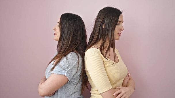 Two women standing with arms crossed gesture and unhappy expression over isolated pink background - Photo, Image