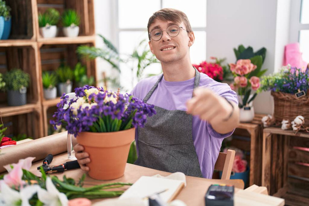 Hombre rubio caucásico trabajando en floristería señalándote a ti y a la cámara con los dedos, sonriendo positivo y alegre  - Foto, Imagen