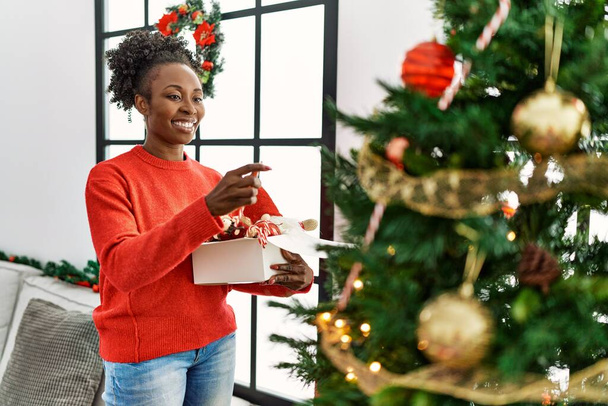 Mujer afroamericana sonriendo confiada decorando árbol de Navidad en casa - Foto, Imagen