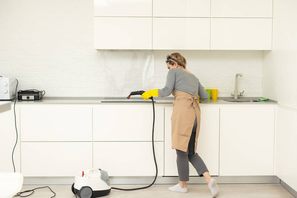 Rajataan kuva naisen yhtenäinen puhdistus suodattimet keittiön alue huppu höyrypuhdistimella, kun hänen miespuolinen kollegansa työskentelee taustalla. Siivouspalvelujen käsite. Kotitaloustyöt
 - Valokuva, kuva