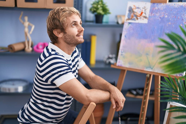Jeune homme artiste souriant confiant assis sur la chaise au studio d'art - Photo, image