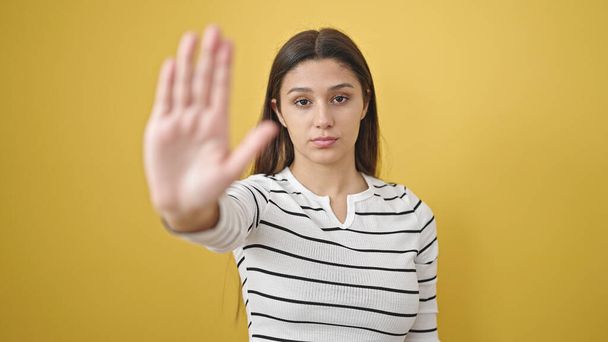 Fiatal gyönyörű spanyol nő csinál stop gesztus kézzel át elszigetelt sárga háttér - Fotó, kép