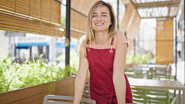 Young blonde woman waitress smiling confident standing at coffee shop terrace - Фото, зображення