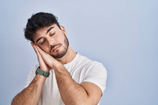 Homme hispanique avec barbe debout sur fond blanc endormi fatigué rêvant et posant les mains ensemble tout en souriant les yeux fermés.  - Photo, image