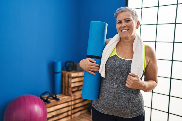 Жінка середнього віку в спортивному одязі, що тримає йогу килимок у спортивному центрі
 - Фото, зображення