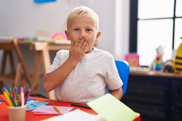 Pieni valkoihoinen poika maalaus koulussa peittää suun kädellä, järkyttynyt ja pelkää erehdystä. yllättynyt ilme  - Valokuva, kuva