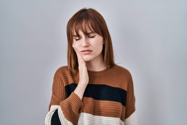 Молодая красивая женщина в полосатом свитере на изолированном фоне касается рта рукой с болезненным выражением лица из-за зубной боли или зубной болезни на зубах. стоматолог  - Фото, изображение