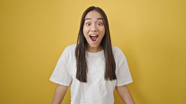 Fiatal gyönyörű spanyol nő áll meglepetés kifejezés felett elszigetelt sárga háttér - Fotó, kép