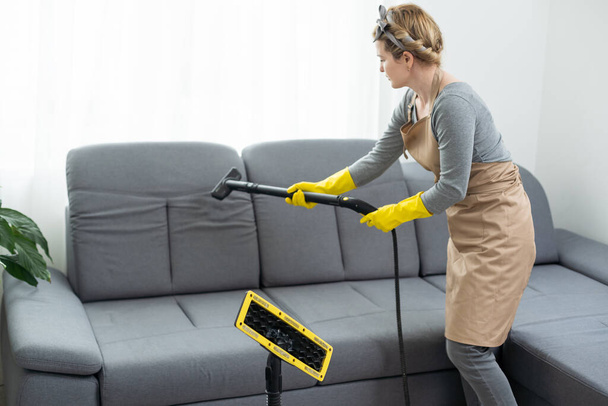 Жінка прибирає диван з пилососом вдома
. - Фото, зображення