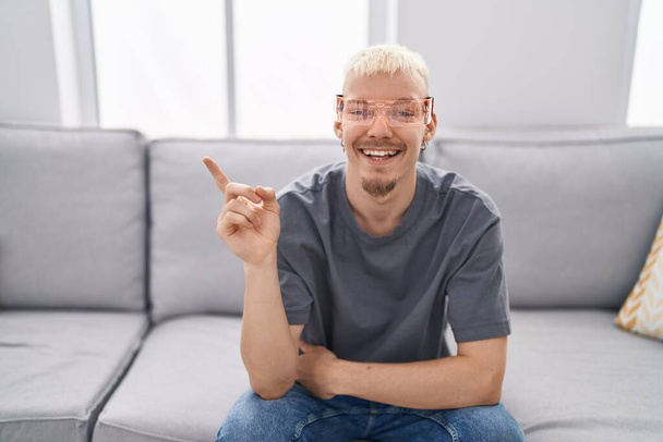 Молодий білий чоловік в окулярах віртуальної реальності посміхається щасливим вказуючи рукою і пальцем на бік
  - Фото, зображення