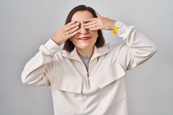 Middle age hispanic woman standing over isolated background covering eyes with hands smiling cheerful and funny. blind concept.  - Photo, Image