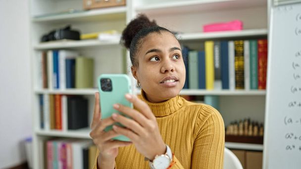 Nuori afrikkalainen amerikkalainen nainen opiskelija käyttää älypuhelinta kirjastossa - Valokuva, kuva
