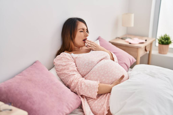 Young pregnant woman yawning sitting on bed at bedroom - Foto, Imagen