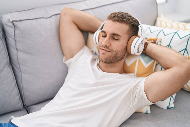 Young caucasian man listening to music lying on sofa at home - Zdjęcie, obraz