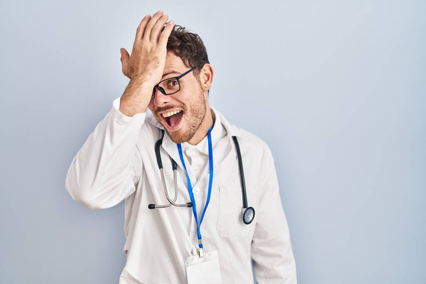 Young hispanic man wearing doctor uniform and stethoscope surprised with hand on head for mistake, remember error. forgot, bad memory concept.  - Fotografie, Obrázek