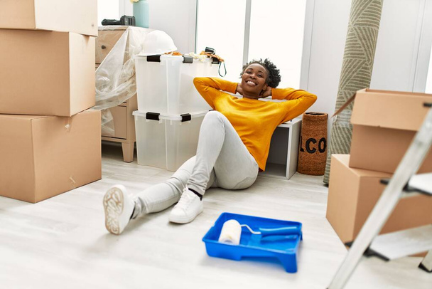 African american woman sitting on floor relaxed with hands on head at new home - Fotoğraf, Görsel
